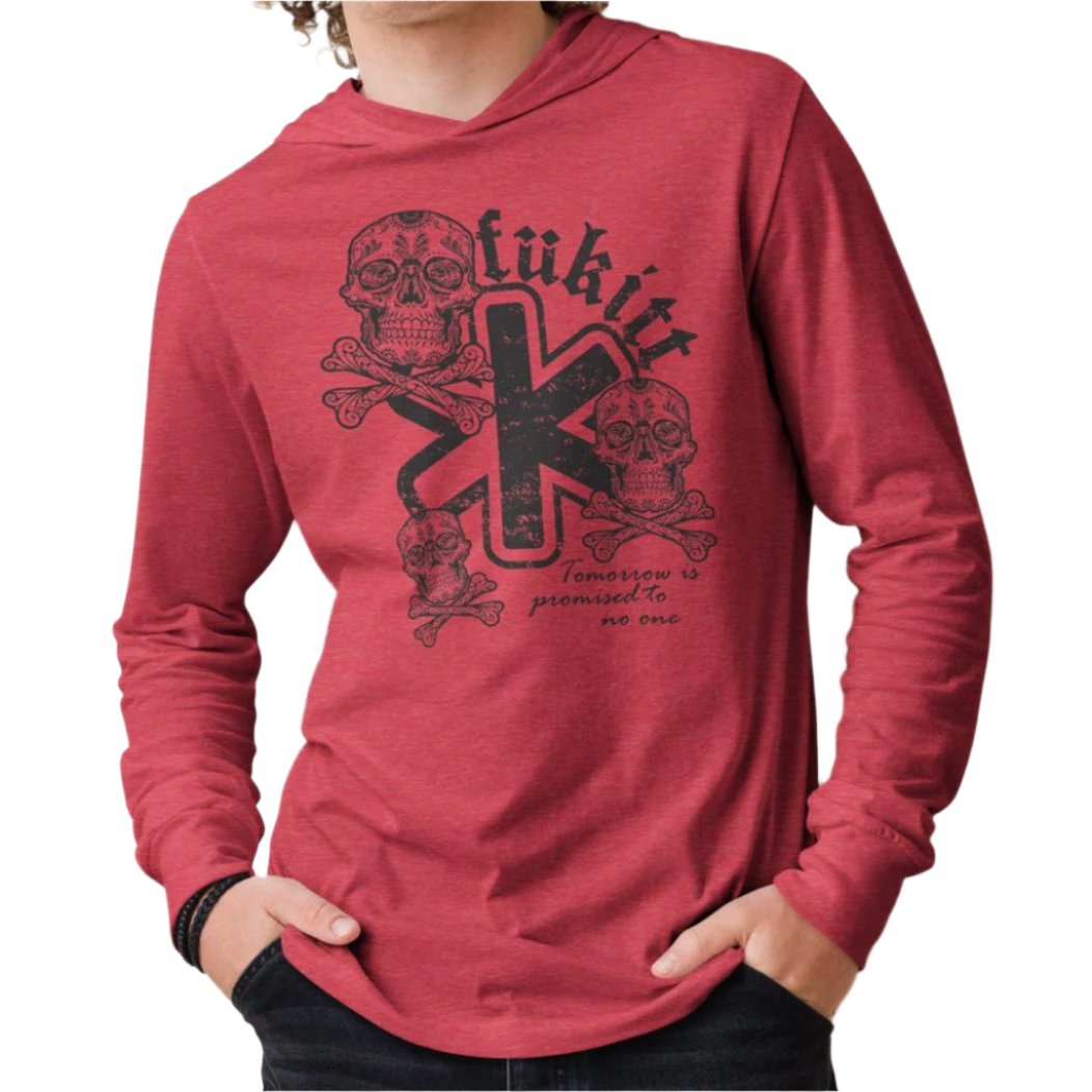 Model wearing the Fükitt Triskull unisex hooded long-sleeve tee in heather red with bold skull and crossbones design featuring the phrase "Tomorrow is promised to no one."